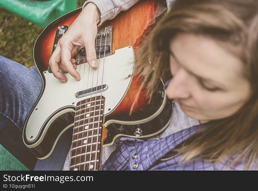 Attractive blonde woman playing a guitar outside in the countryside.