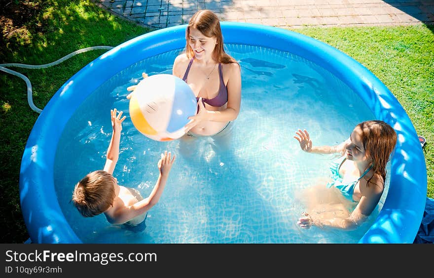 Top view of happy cheerful children with mother playing volleyball in inflatble swimming pool at house backyard garden