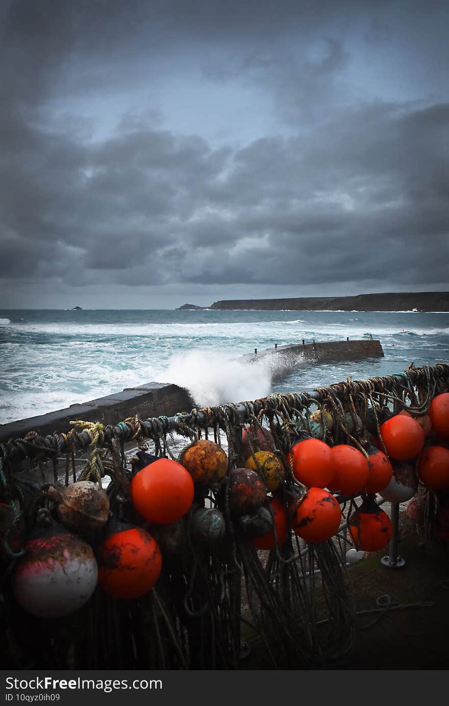 Foaming seas and storm clouds at Sennen Cove with large waves around the harbour wall, West Cornwall England UK. Bythe wall are the fishermen`s equipment like ropes and buoys and shellfish pots. Foaming seas and storm clouds at Sennen Cove with large waves around the harbour wall, West Cornwall England UK. Bythe wall are the fishermen`s equipment like ropes and buoys and shellfish pots