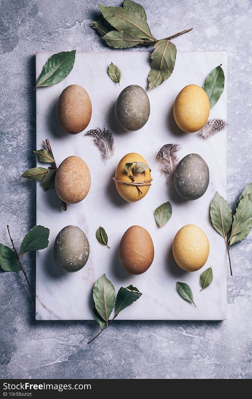 Happy easter concept. Multicolored easter painted eggs and branches with leaves on a white marble cutting board on a gray