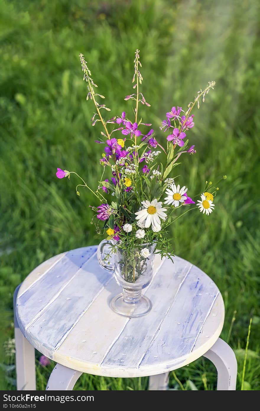 Bouquet of wild flowers in a glass vase on a rough wooden white bench, summer concept, farm rustic concept