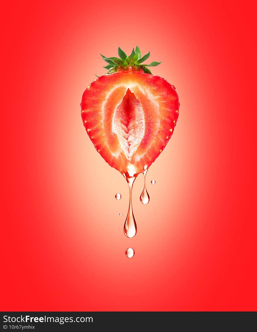 A drop of juice drips from half a strawberry on a red background