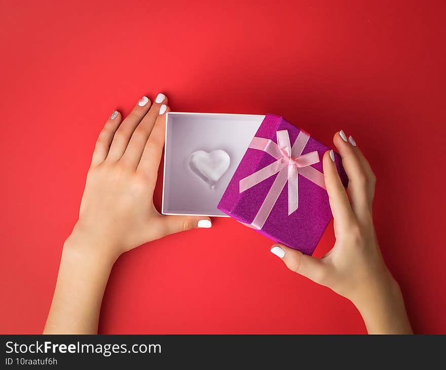 The girl`s hands open a gift box with a glass heart inside