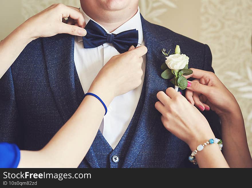 female hands adjust the groom s bow tie and boutonniere. preparing the groom  morning  hands  close-up