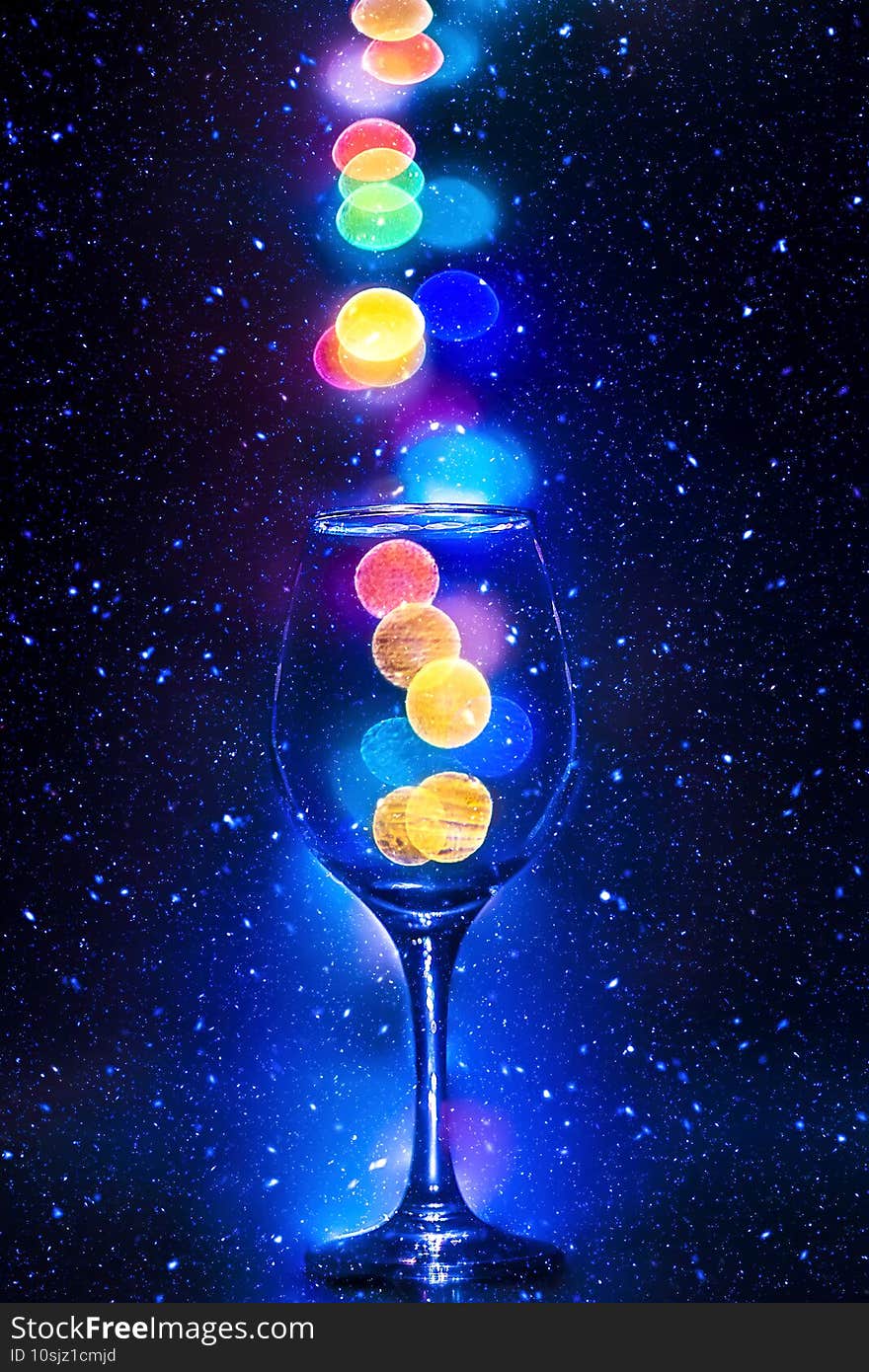 Abstract composition with colorful bokeh falling into wine glass on blue stars background. Galaxy or space theme. Abstract composition with colorful bokeh falling into wine glass on blue stars background. Galaxy or space theme.