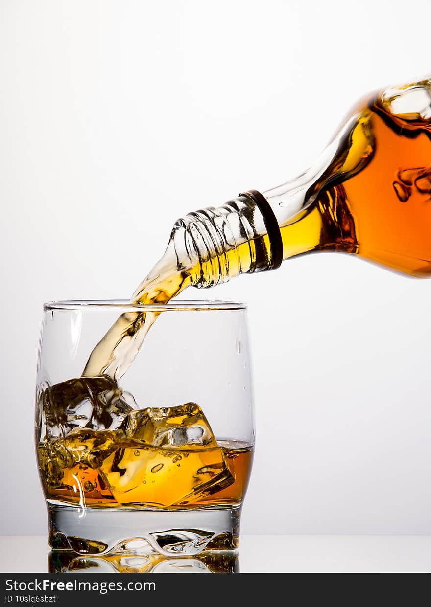 Pouring whisky from a bottle into a tumbler on white background