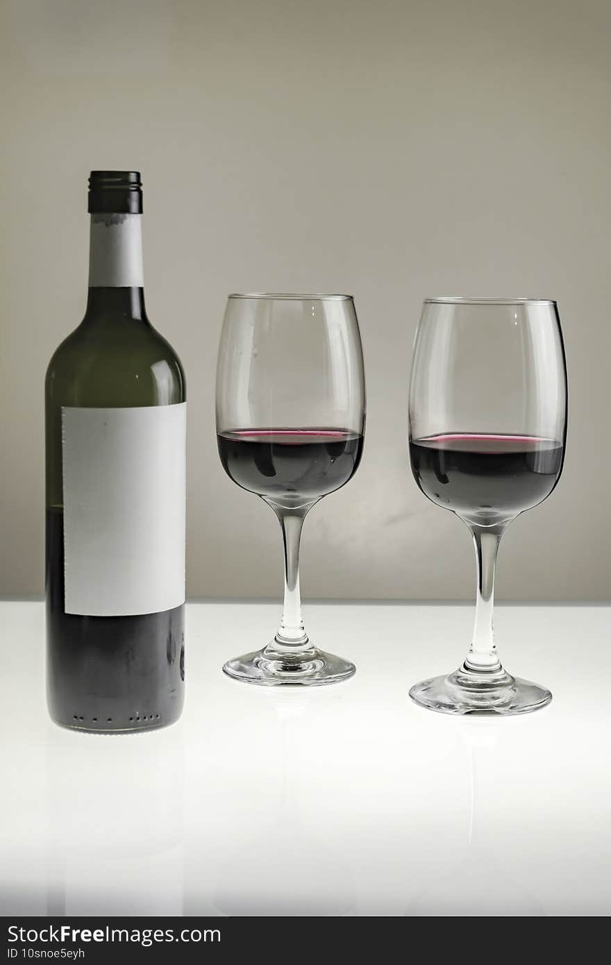 Two glasses and a bottle of red wine on a blurred homogeneous background