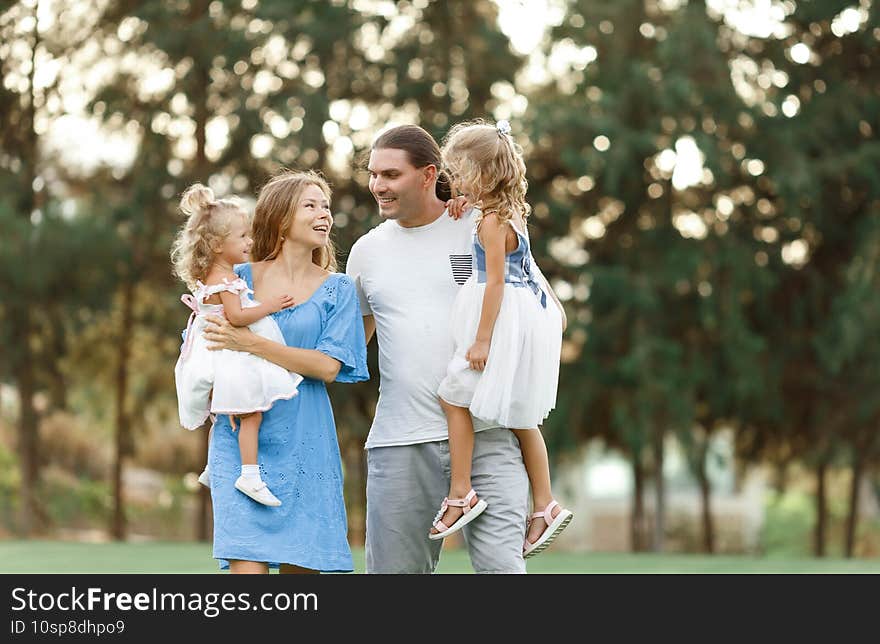 Parents hold daughters in their arms In Countryside  enjoing time together. Happy family concept. Blurred trees background. Perfect family