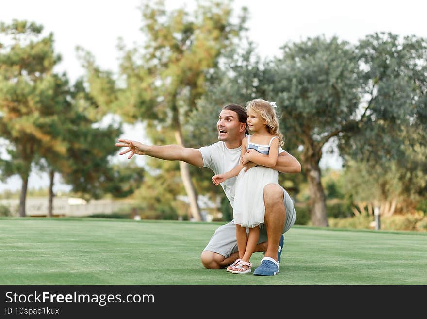 Portrait of a happy caring father teaching his small pretty daughter how launching a toy plane in a green park  smiling