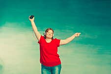 Young Attractive Plump Woman With Red Hair And Jeans Jumping And Fooling Around And Dancing In Headphones On A Blue Background Royalty Free Stock Image