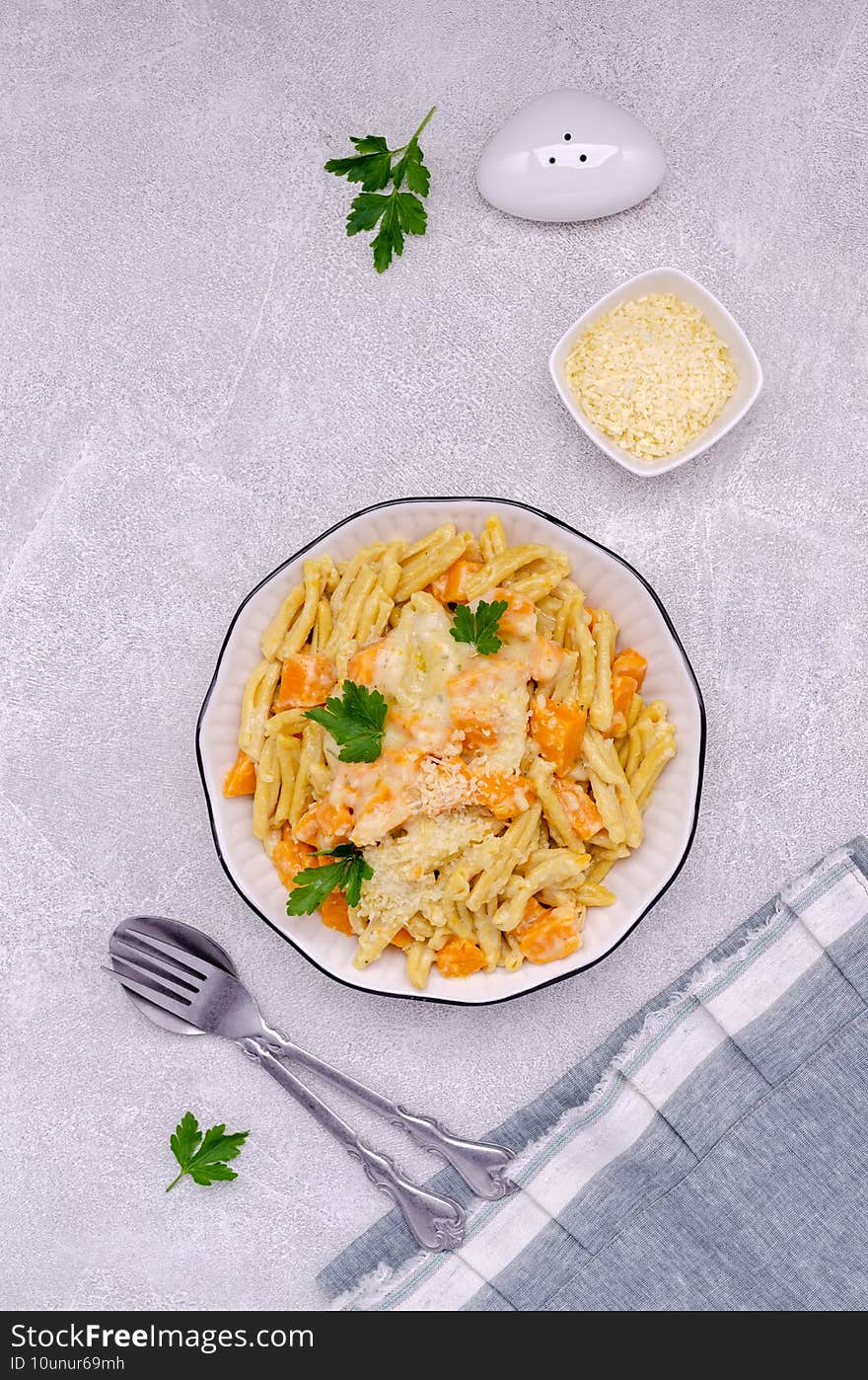 Pasta with pumpkin in white sauce in a ceramic dish on a stone background. Selective focus