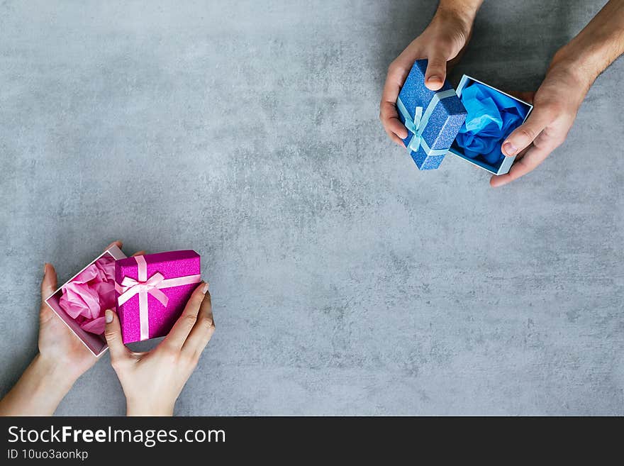 Protection from Covid-19. Male and female hands hold pink and blue gift boxes with gloves inside on the copy space. Advertising background. Congratulations on the anniversary. Valentine's Day