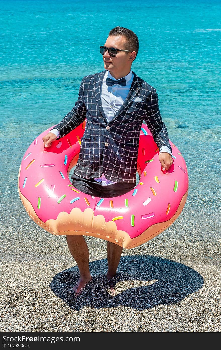 Happy businessman in a jacket with an inflatable donut on a tropical beach. Summer vacation concept.