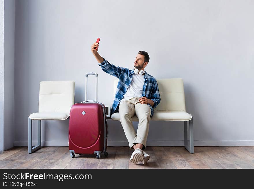 Man in headphones taking selfie with smartphone near suitcase in airport. Man in headphones taking selfie with smartphone near suitcase in airport