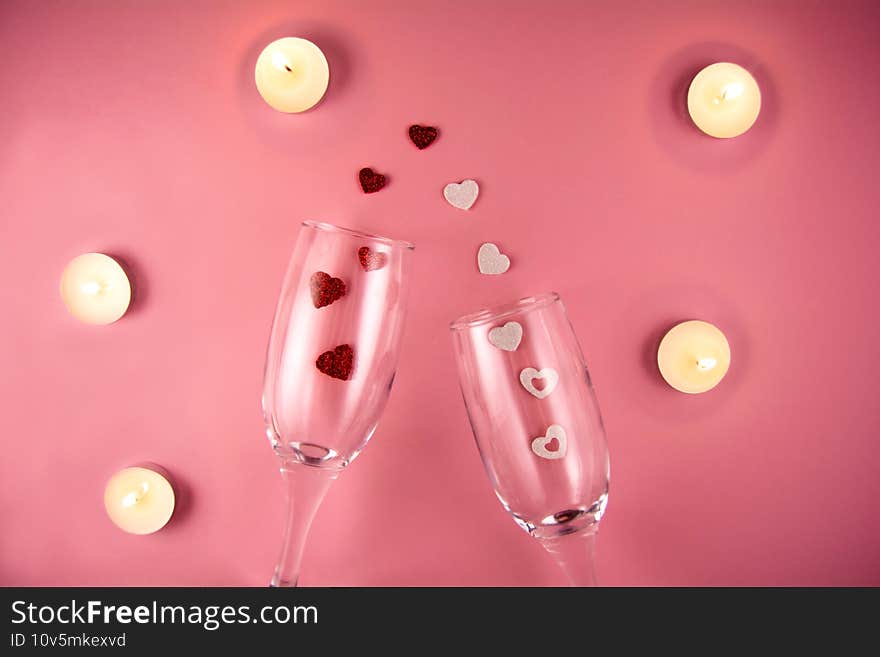 Two glasses with splash of red and white heart and burning candles on a pink background.