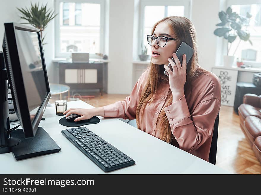 Female office worker uses her phone sitting at table with computer