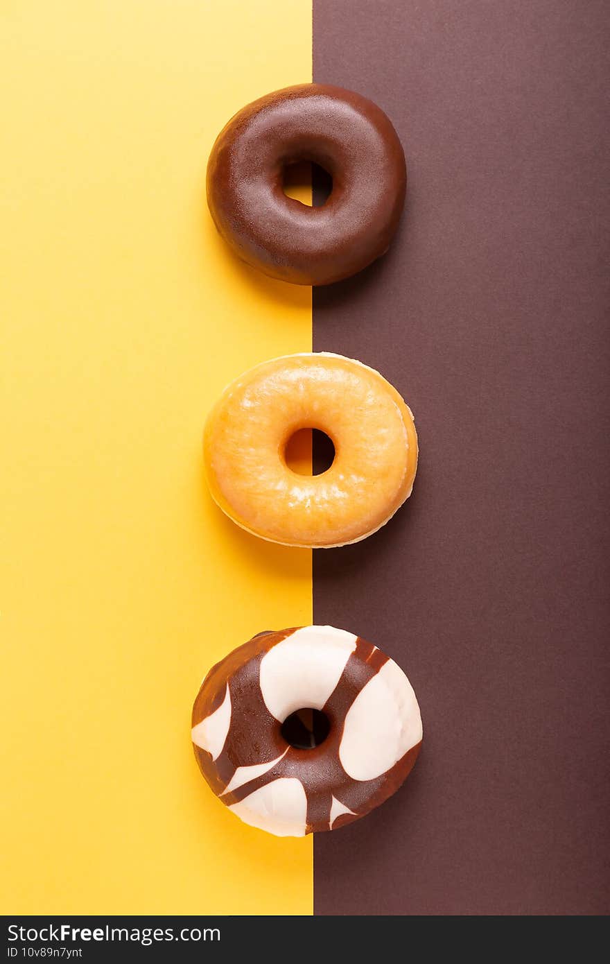 Flat lay composition of three donuts on brown and yellow background. vertical format