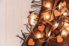 Paper Hearts And A Glowing Garland Are On A Brown Fringed Scarf On A Light Wooden Background. Stock Photography