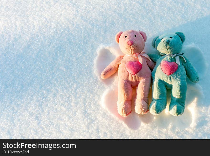 Two small teddy bears are makes a snow angel on a snow.Winter sunny evening.Copy space