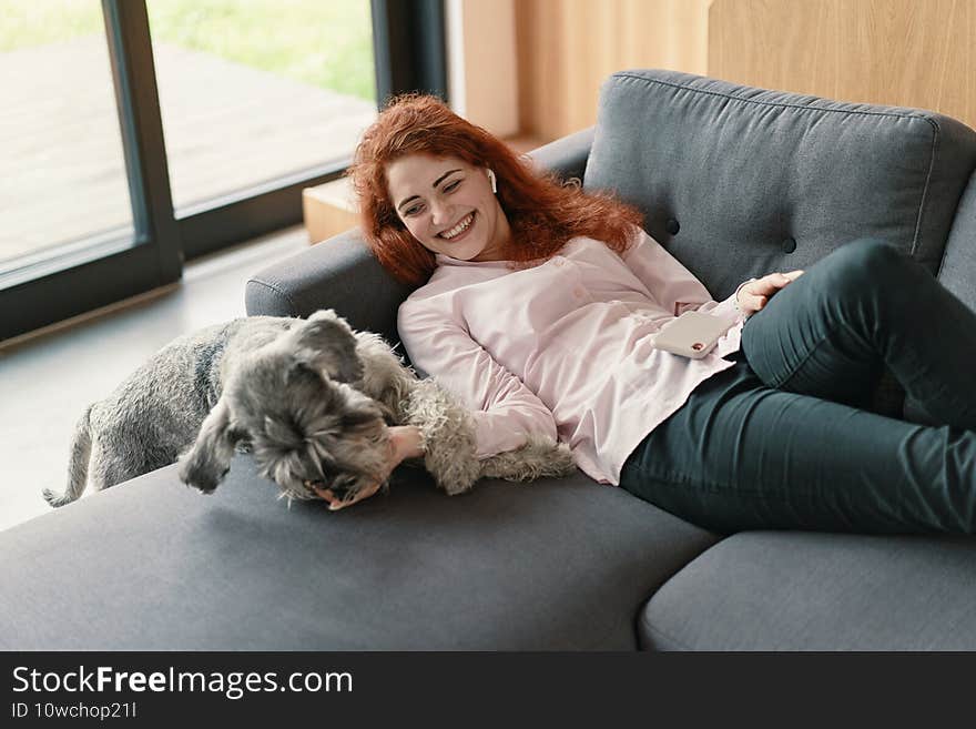 Woman resting on a sofa laughing and cuddling a dog