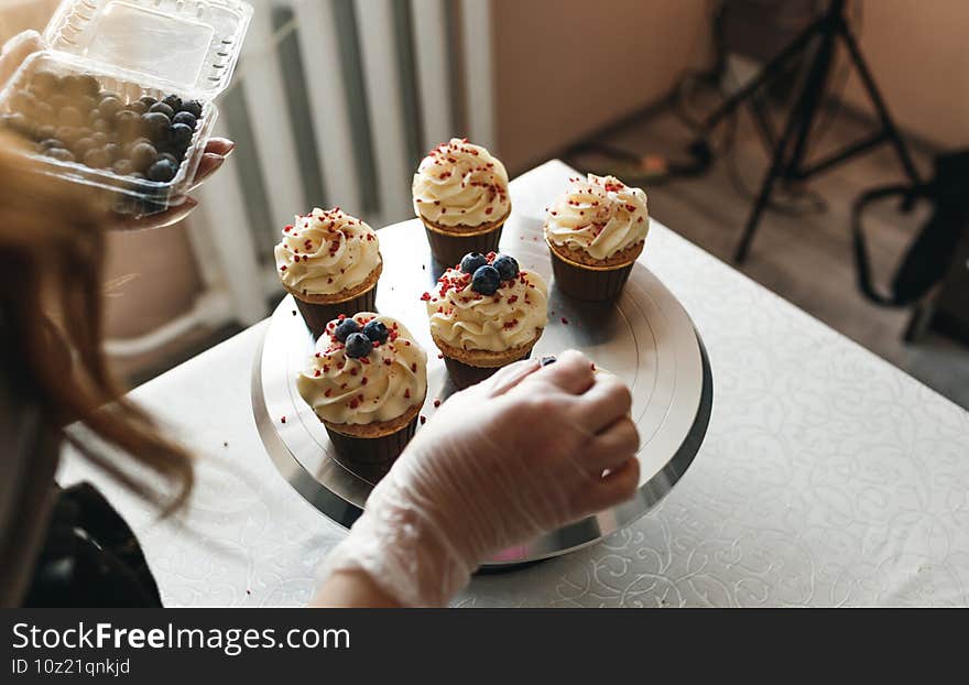 the chef girl decorates fresh cakes covered with vanilla cream with berries.Sweet homemade cupcakes with cream on a tray