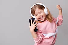 A Little Girl Blogger Influencer Records A Blog Video On A Smartphone, Dances And Listens To Music With Headphones On A Stock Photography