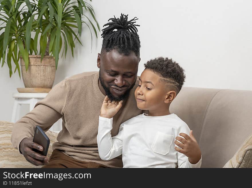 Father and son, dark skinned African, taking selfie at home