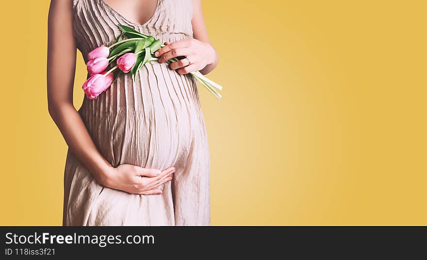 Beautiful pregnant woman with tulips flowers holds hands on belly in white background. Young woman in maternity dress waiting for baby birth. Pregnancy, Motherhood, Mother`s Day Holiday concept. Beautiful pregnant woman with tulips flowers holds hands on belly in white background. Young woman in maternity dress waiting for baby birth. Pregnancy, Motherhood, Mother`s Day Holiday concept