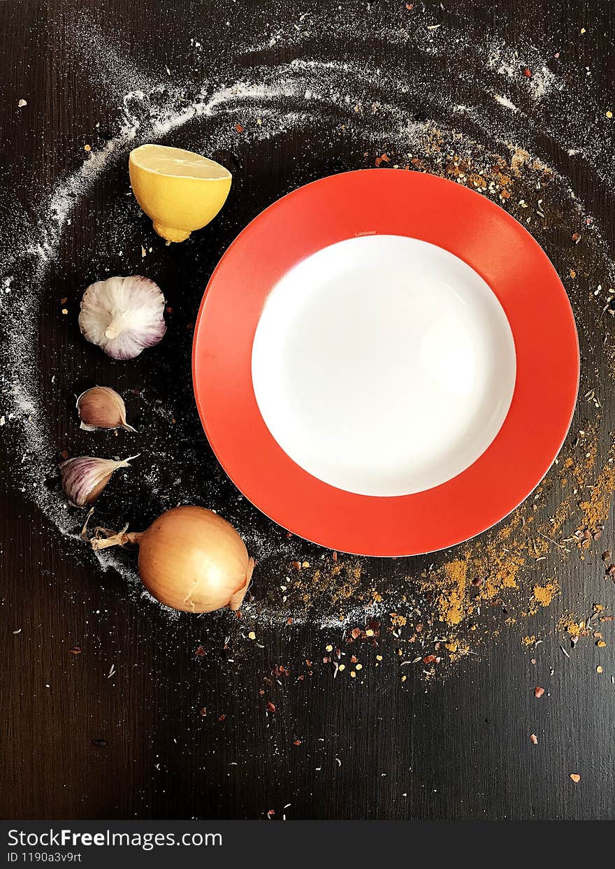 a white and red round plate on a black table decorated with spices.