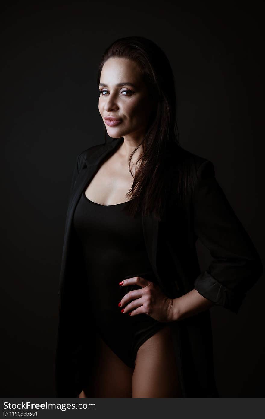 Portrait of a beautiful woman in a black bodysuit and jacket posing on a dark background