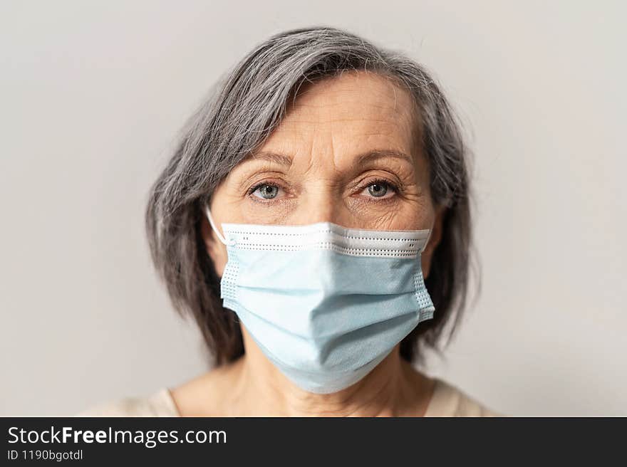 Close-up an elderly mature grey-haired woman wearing protective face mask and looking at the camera intently, isolated. Concept of safety and social distance during coronavirus pandemic. Close-up an elderly mature grey-haired woman wearing protective face mask and looking at the camera intently, isolated. Concept of safety and social distance during coronavirus pandemic
