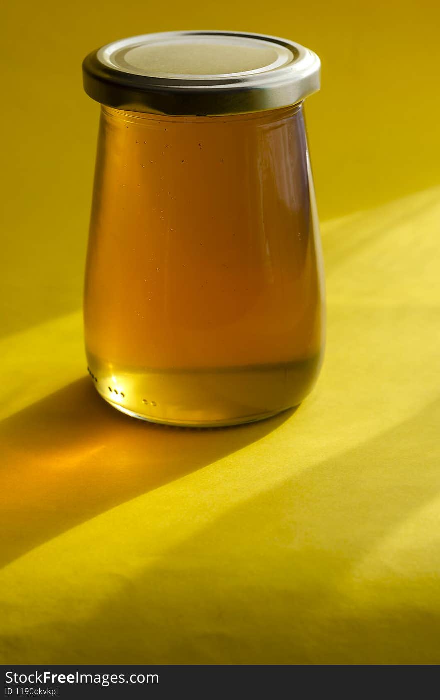 Natural sugar substitute, healthy food concept. Raw bee honey in glass jar on yellow background.  Close-up of liquid organic honey. Selective focus
