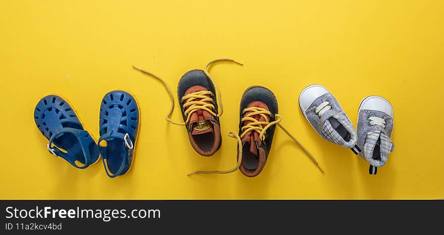 Baby first steps. Three pairs of boy blue shoes variety on yellow color background, top view. Kids footwear, beach sandals, booties and soft infant shoes in a row. Baby first steps. Three pairs of boy blue shoes variety on yellow color background, top view. Kids footwear, beach sandals, booties and soft infant shoes in a row