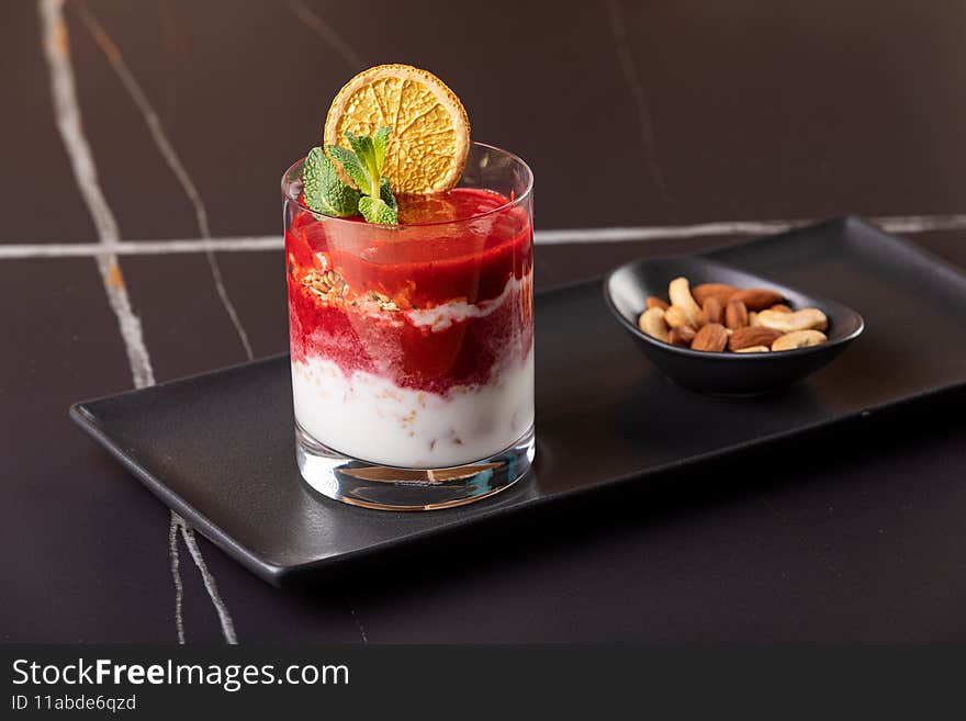 Layered dessert with fruits, nuts and cream cheese in glass on black background