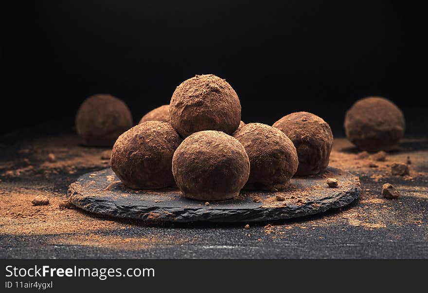 Chocolate truffles, round chocolate candies on black slate background with cocoa powder. Chocolate truffles, round chocolate candies on black slate background with cocoa powder