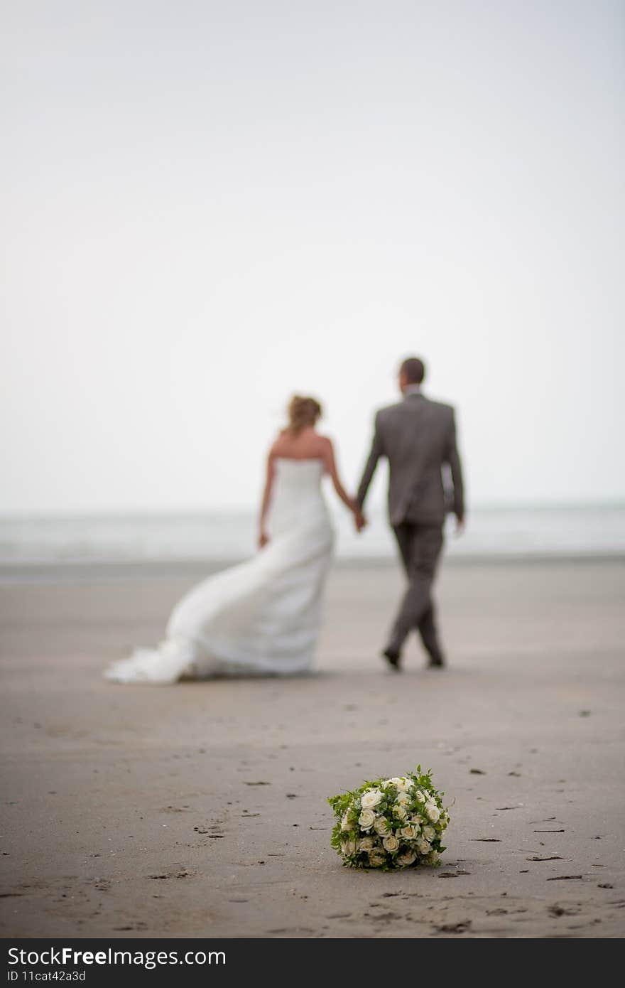 Out of focus and unrecognizable bride and groom walking away on the beach