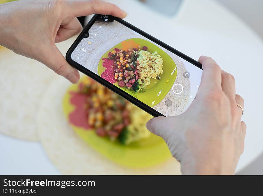 Photographing food on a smartphone. Yellow plate with rice and vegetables. Healthy natural food Photographing food on a smartphone. Yellow plate with rice and vegetables. Healthy natural food