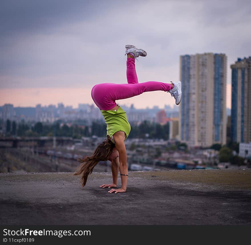 Flexible girl keep balance on hands on the cityscape background . Concept of creativity, balance and individuality.