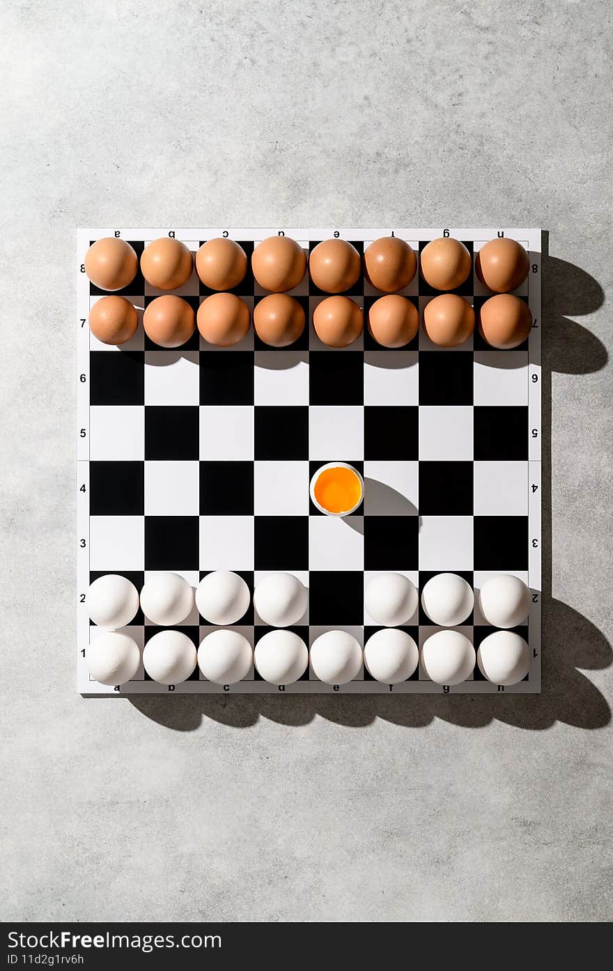 From above view on a chessboard with figures of white and brown eggs on a gray background