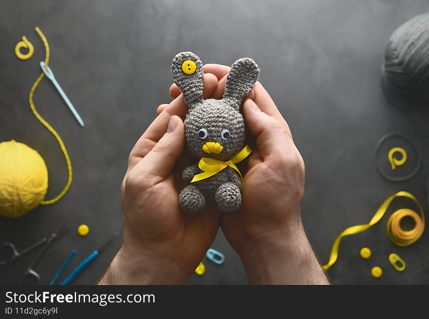 DIY Easter gift making theme. Human hands hold handmade knitted toy Easter rabbit and needlework accessories