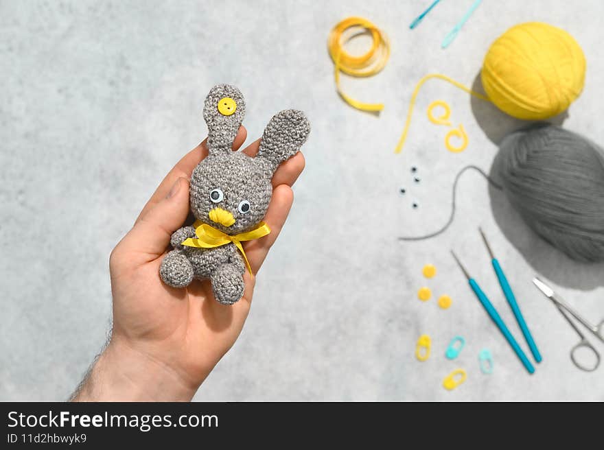 DIY Easter gift making theme. Human hands hold handmade knitted toy Easter rabbit and needlework accessories