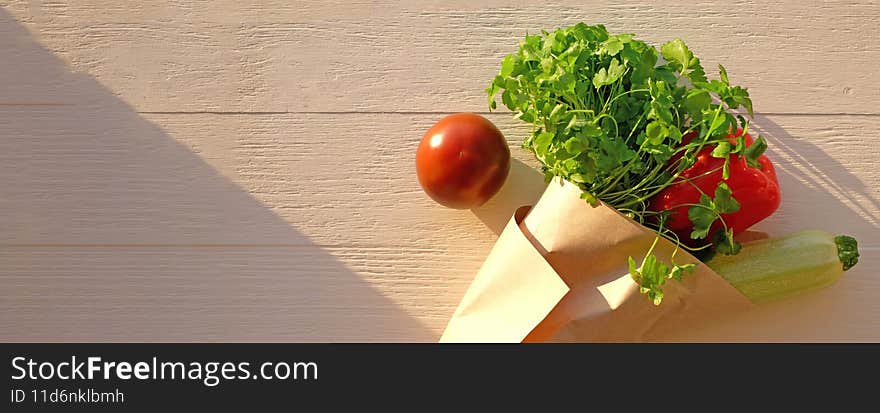 Fresh vegetables in craft paper as bouquet on wooden background, sunlight, top view. Healthy food concept. Banner, copy space.