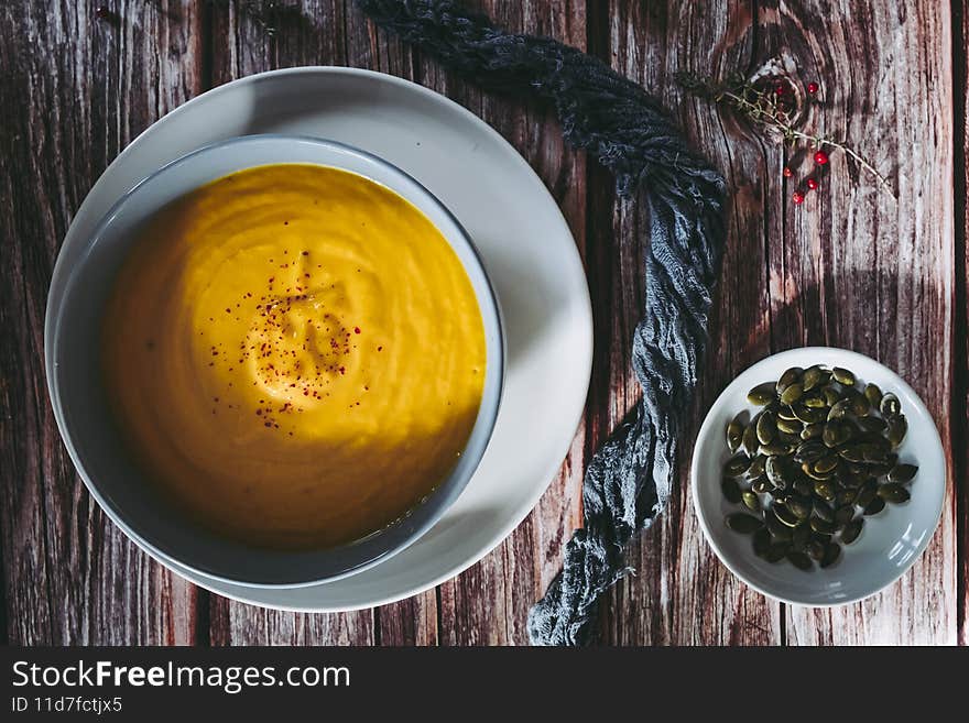 Pumpkin and carrot soup with pink berries in a bowl on a wooden kitchen table - Healthy homemade food