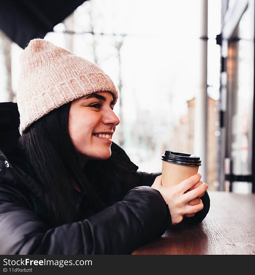 Girl smiling, holds paper cup of coffee in hand near cafe. Blurred background. High quality photo