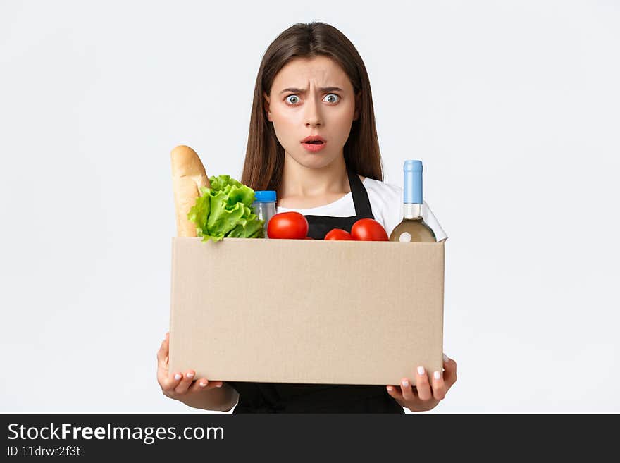 Employees, delivery and online orders, grocery stores concept. Shocked and confused female cashier, saleswoman holding