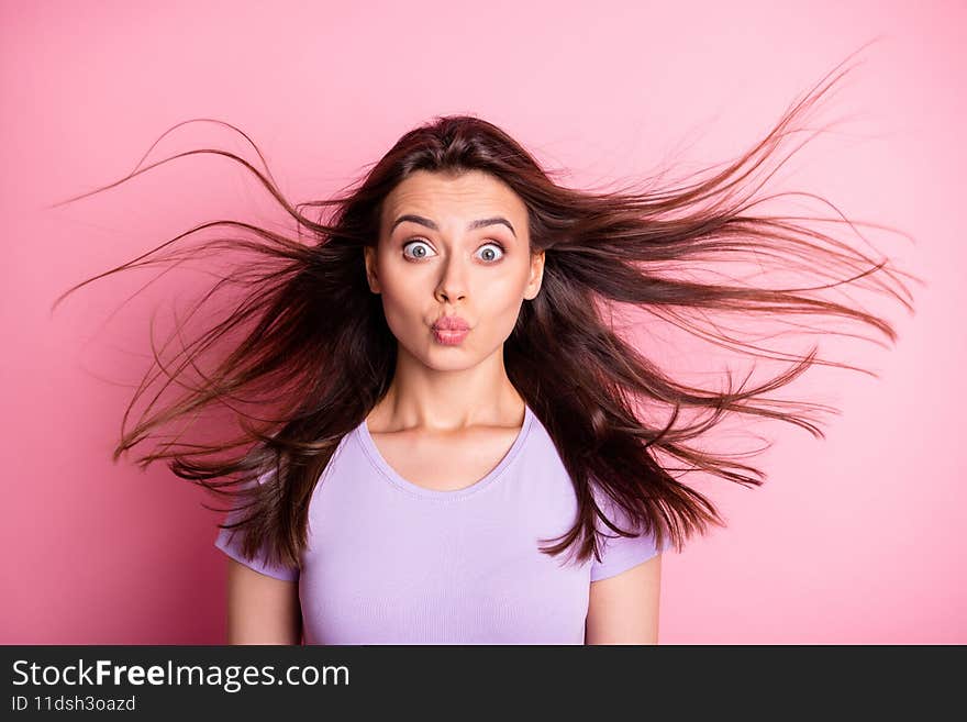 Portrait of flirty pretty girl in purple t-shir blowing kiss flowing hair dressed casual  on pink color background.