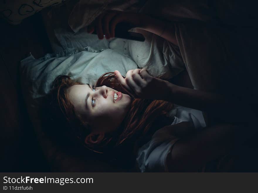 woman with a phone in her hands at night lying in bed rest before bedtime