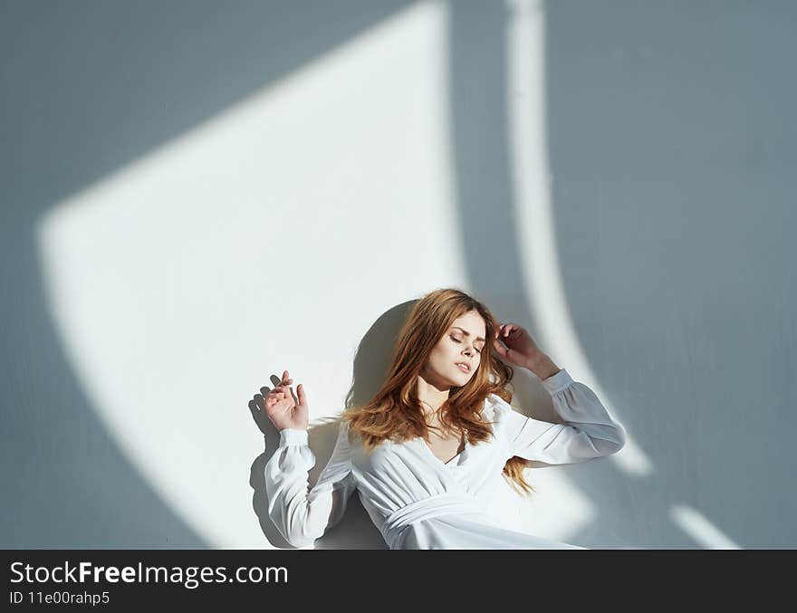 Woman model is leaning against the wall a falling shadow of a white sundress room. High quality photo