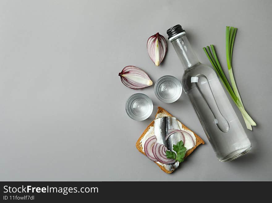Bottle and shots of vodka, and snacks on gray background