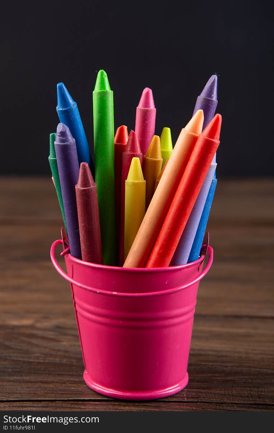 colored crayons on the wooden table, blackboard background